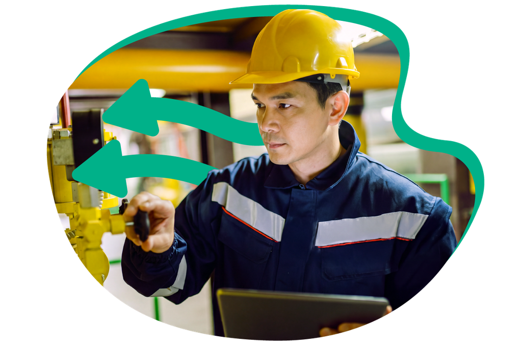 A worker in a hard hat and reflective uniform inspects gas machinery, holding a tablet.