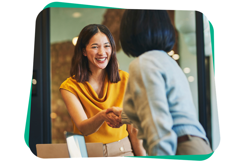 Smiling woman in a yellow blouse shakes hands with a colleague in an office setting.