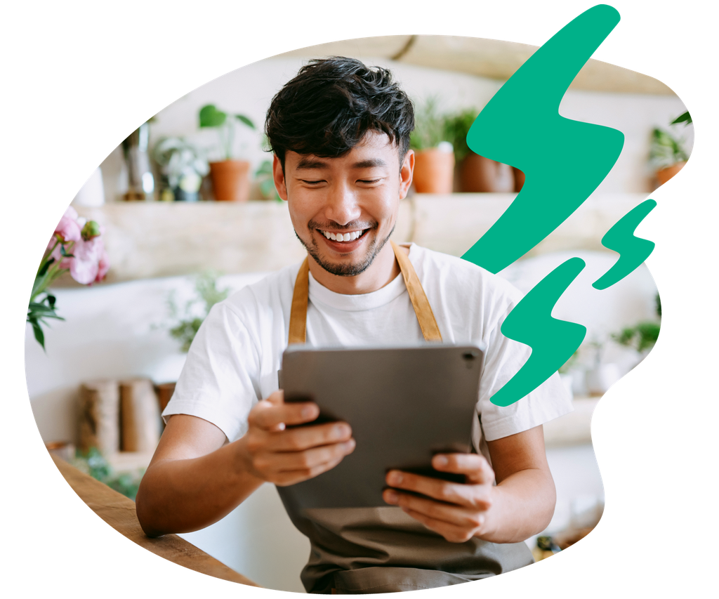Smiling man in an apron holds a tablet in a plant-filled room, with a decorative teal lightning bolt shape beside him.