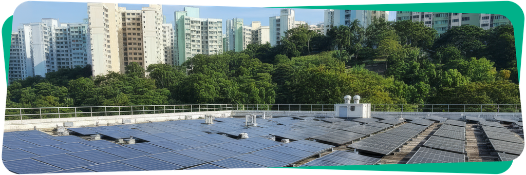 Solar panels on a rooftop with high-rise buildings in the background and lush green trees in between, under a clear blue sky.